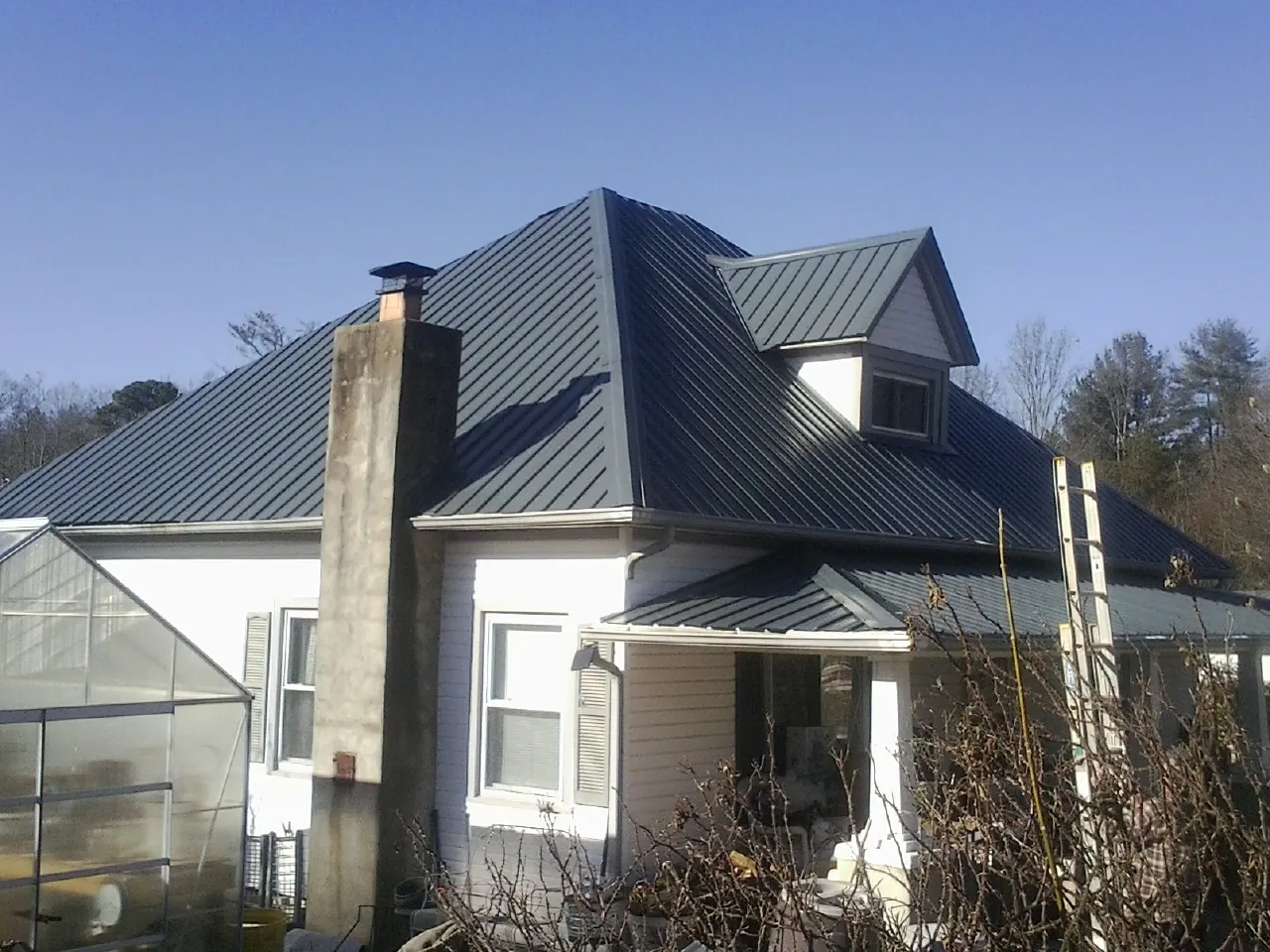 Dark blue standing seam metal roof on a white farmhouse with dormer — Slate & Tile Roof Repair by Roofing Brothers in Dowling