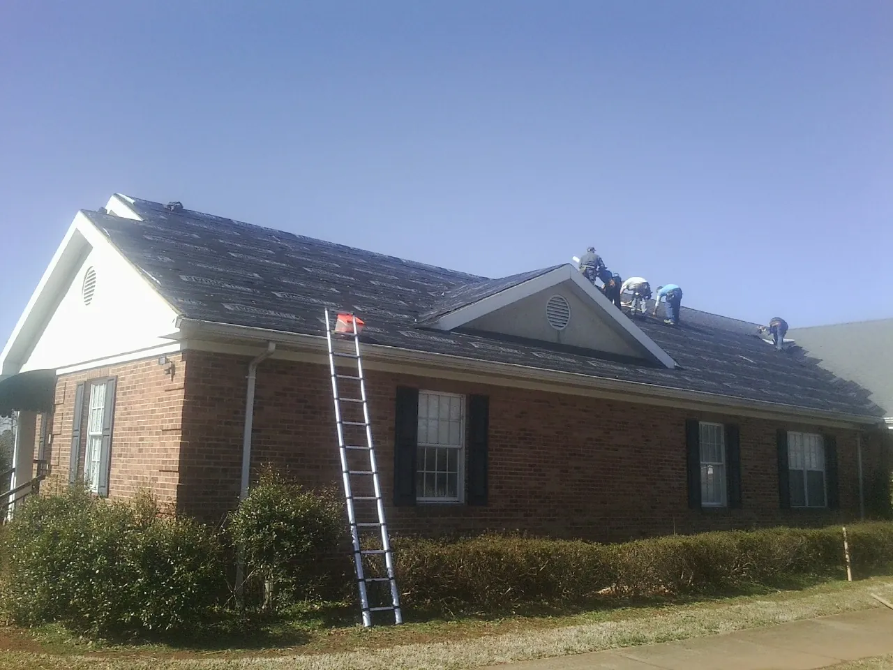 Crew tearing shingles off a brick ranch roof with a ladder set — Metal Roof Repair work by our crew in Dowling