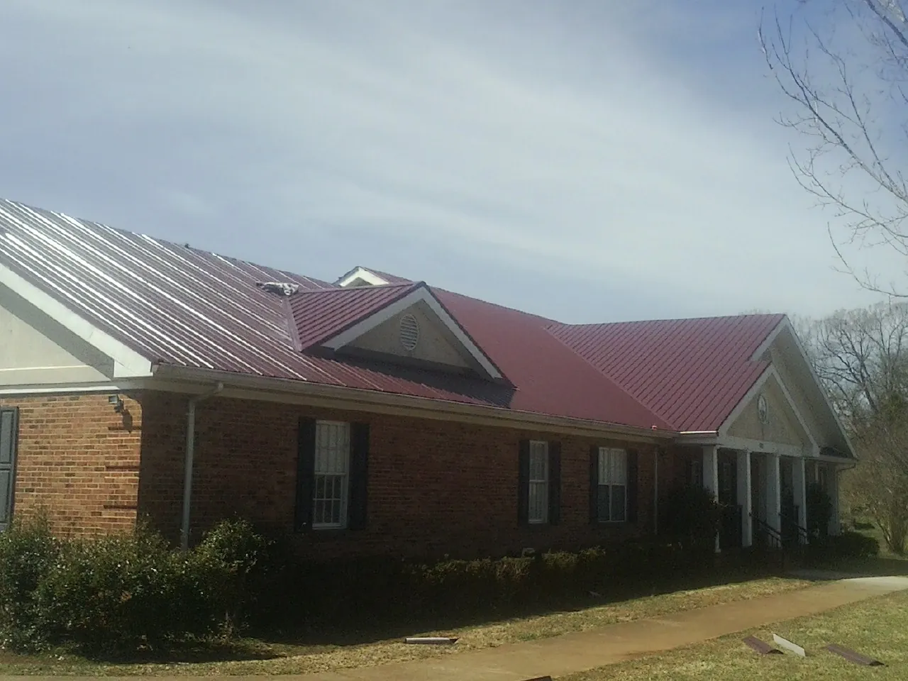 Red metal roof with gabled entries on a long brick building, from a Hail Damage Roof Repair job in Dowling