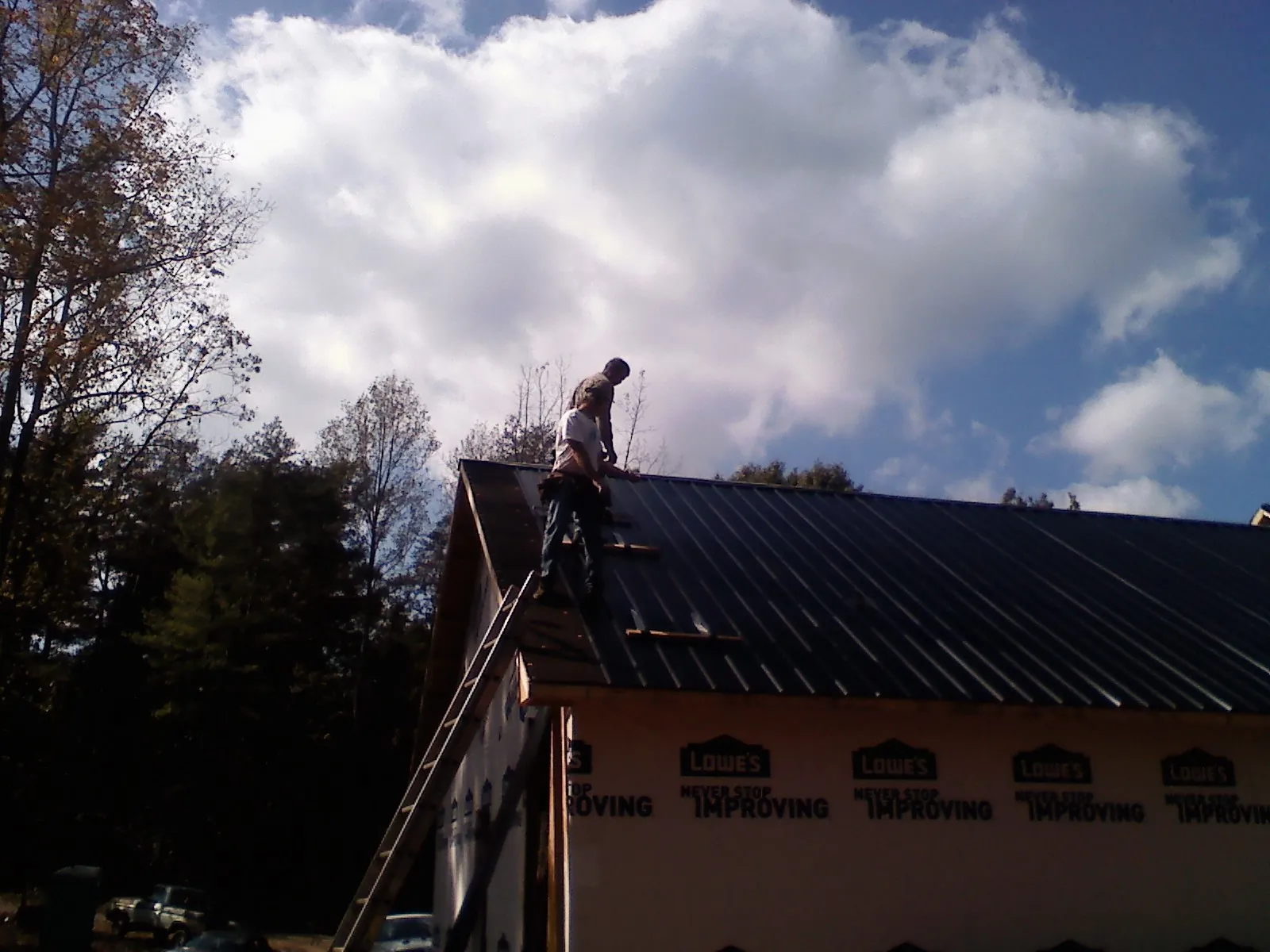 Roofer fastening dark metal panels high against a cloudy sky, from a Roof Inspection job in Dowling