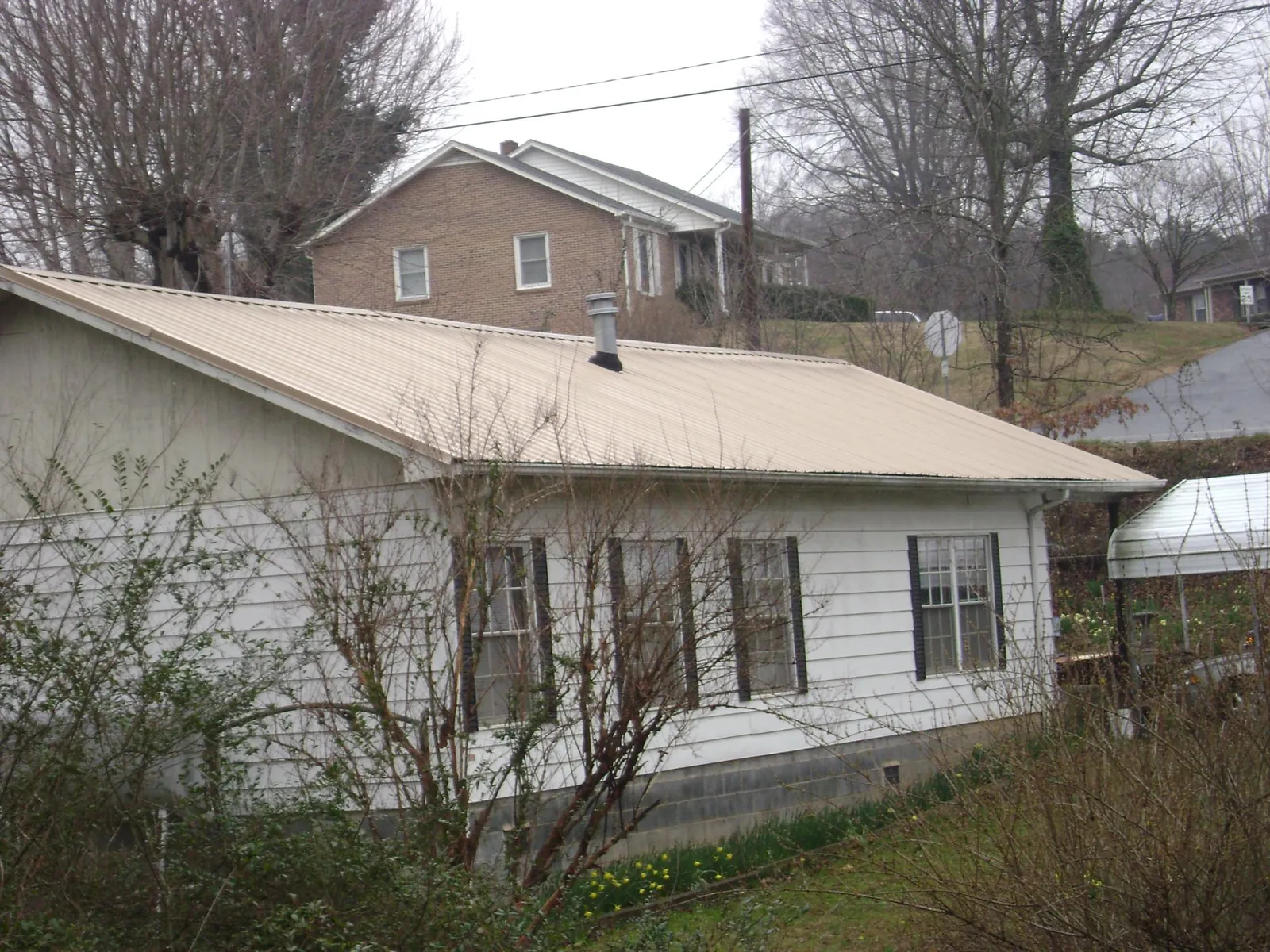 Tan metal roof on a white sided house set into a hillside — Commercial Roofing by Roofing Brothers in Dowling